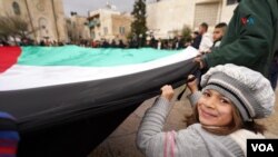 Una niña sostiene, junto a decenas de personas una gigantesca bandera de Palestina, en la plaza central de la ciudad de Belén, que este año no festejará la Navidad en homenaje a los miles de fallecidos en Gaza.