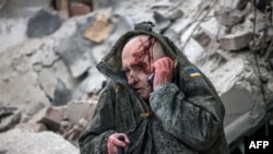 An injured man talks on a mobile phone after he was rescued by emergency workers from a partially destroyed residential building following a shelling in Sloviansk, on April 14, 2023, during the Russian invasion of Ukraine.