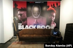 Seorang pria membaca pesan di ponselnya di bawah poster film The Black Book di Lagos Nigeria, Jumat, 20 Oktober 2023. (Foto: AP/Sunday Alamba)