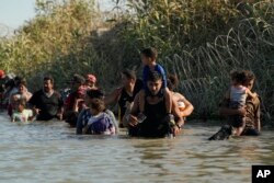 Para pria dan perempuan migran menggendong anak-anak mereka untuk menyeberangi sungai Rio Grande, setelah menyeberang dari Meksiko ke AS, 1 Agustus 2023, di Eagle Pass, Texas.