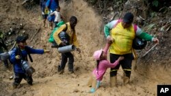 FILE - A woman lifts a child from a muddied path as Ecuadorian migrants walk across the Darien Gap from Colombia into Panama, hoping to reach the U.S., on Oct. 15, 2022.