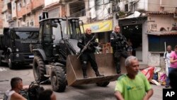 Police ride past residents in a bulldozer they use to clear street barricades during a security operation against organized crime in the Mare Complex favela of Rio de Janeiro, Brazil.