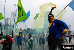 Seorang buruh mengacungkan asap saat mengikuti aksi protes terhadap Undang-Undang Cipta Kerja atau yang dikenal dengan istilah 'omnibus law', di luar gedung Mahkamah Konstitusi, di Jakarta, 2 Oktober 2023. (Foto: REUTERS/Willy Kurniawan)