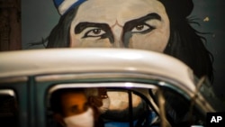 ARCHIVO - En plena pandemia del Covid, doersonas con mascarillas pasan a bordo de un auto frente a un mural de Ernesto "Che" Guevara en La Habana, en abril de 2020.