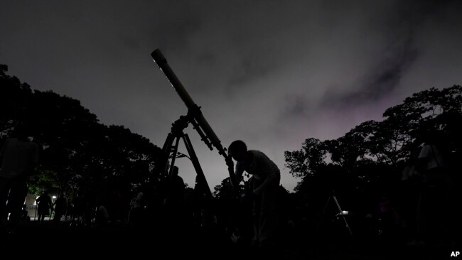 FILE - A girl looks at the moon through a telescope in Caracas, Venezuela, May 15, 2022. Mercury, Jupiter, Venus, Uranus and Mars will gather near the moon in a planet parade this week. The best day to catch the whole group will be Tuesday after sunset.