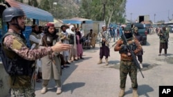 FILE - A Pakistani paramilitary soldier, left, and Taliban fighters stand guard on their respective sides at a border crossing point between Pakistan and Afghanistan, in Torkham, in Khyber district, Pakistan, Sept. 5, 2021. 