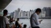 Orang-orang duduk di sepanjang kawasan pejalan kaki di sebelah pelabuhan Victoria di Hong Kong pada 31 Agustus 2023, sehari sebelum datangnya Topan Saola. (ISAAC LAWRENCE / AFP)