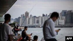 Orang-orang duduk di sepanjang kawasan pejalan kaki di sebelah pelabuhan Victoria di Hong Kong pada 31 Agustus 2023, sehari sebelum datangnya Topan Saola. (ISAAC LAWRENCE / AFP)