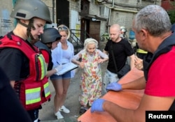 People and medical workers help a local resident as she leaves the site of a residential building damaged during a Russian air strike in Kharkiv, Ukraine, June 22, 2024.