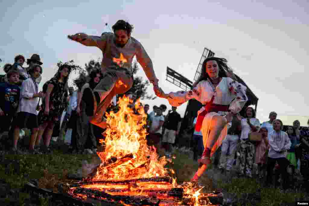 People jump over a campfire during a celebration on the traditional Ivana Kupala (Ivan the Bather) holiday in the village of Vytachiv in Kyiv region, Ukraine, amid Russia&#39;s attack on Ukraine, June 22, 2024. The ancient tradition, originating from pagan times, is marked with grand overnight festivities during which people sing and dance around campfires, believing it will purge them of their sins and make them healthier