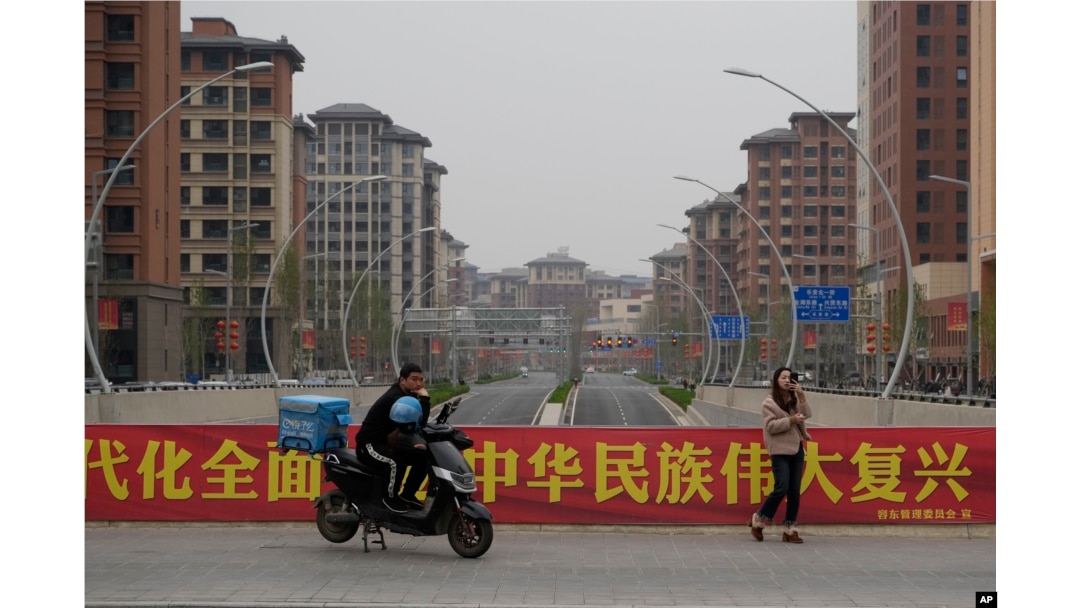 中国河北雄安街头一名快递小哥在口号横幅前休息。(2023年4月1日)