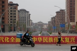 中国河北雄安街头一名快递小哥在口号横幅前休息。（2023年4月1日）