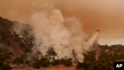 A water-dropping helicopter drops on flames from the advancing Lake Fire in Los Olivos, Calif., July 6, 2024. 