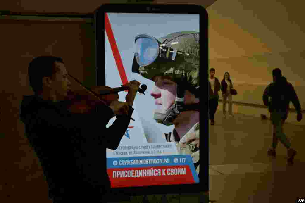 A street musician plays his violin by an advertising screen promoting contract military service in the Russian army at the Moscow metro.