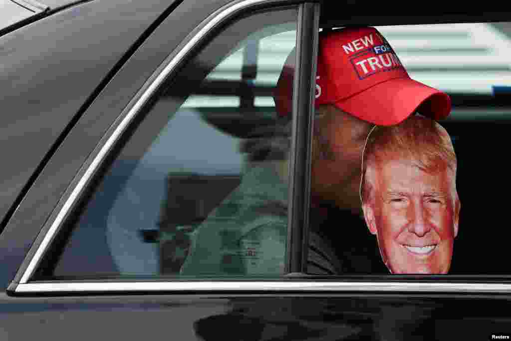 Un hombre se pasea en un vehículo cerca de la Corte luciendo una máscara con la cara de Trump y una gorra de su actual campaña presidencial.