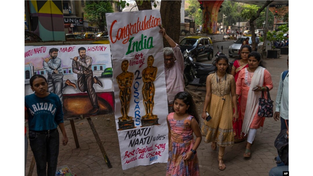 Orang-orang berjalan melewati lukisan yang dibuat oleh seniman untuk merayakan kemenangan dua penghargaan Oscar di Mumbai, India, Senin, 13 Maret 2023. India merayakan dua Penghargaan Akademi bersejarahnya dengan antusiasme yang sesuai dengan lagu orisinal terbaik berenergi tinggi "Naatu Naatu."( AP Photo/Rafiq Maqbool)