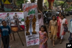 Orang-orang berjalan melewati lukisan yang dibuat oleh seniman untuk merayakan kemenangan dua penghargaan Oscar di Mumbai, India, Senin, 13 Maret 2023. India merayakan dua Penghargaan Akademi bersejarahnya dengan antusiasme yang sesuai dengan lagu orisinal terbaik berenergi tinggi "Naatu Naatu."( AP Photo/Rafiq Maqbool)
