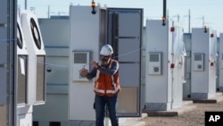 FILE - A worker walks at Orsted's Eleven Mile Solar Center lithium-ion battery storage energy facility, Feb. 29, 2024, in Coolidge, Ariz. Batteries allow renewables to replace fossil fuels while keeping a flow of power when wind or solar are not producing. 