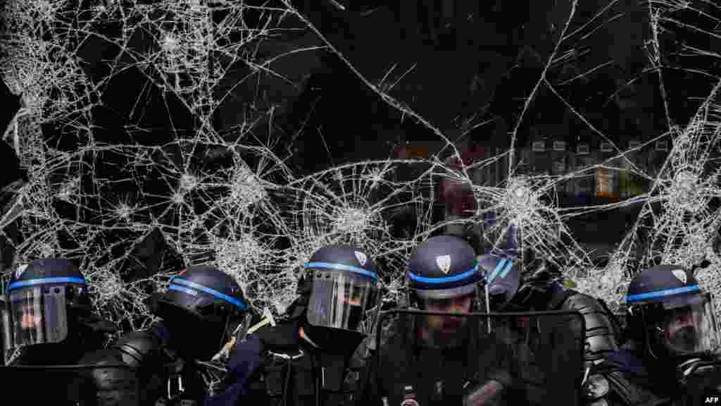 Полицајците стојат пред скршен излог на продавница за време на демонстрациите во Лион, источна Франција.
