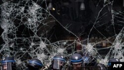 Police officers stand in front of the broken window of a shop during a demonstration on May Day to mark the international day of the workers in Lyon, France.