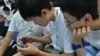 资料照片：2023年8月17日，在北京举行的年度世界机器人大会上，一名学生帮助他的同学通过智能手机玩网络游戏。（美联社照片）
