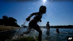 Judah Boyle, of Des Moines, Iowa, splashes water as he runs on the beach at Gray's Lake Park, Aug. 26, 2024, in Des Moines, Iowa. 