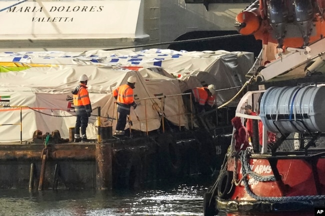 Staffers of port, left, stand on the aid platform and Open Arms aid group on the ship as it prepares to ferry some 200 tons of rice and flour directly to Gaza, at the port in Larnaca, Cyprus, March 10, 2024.