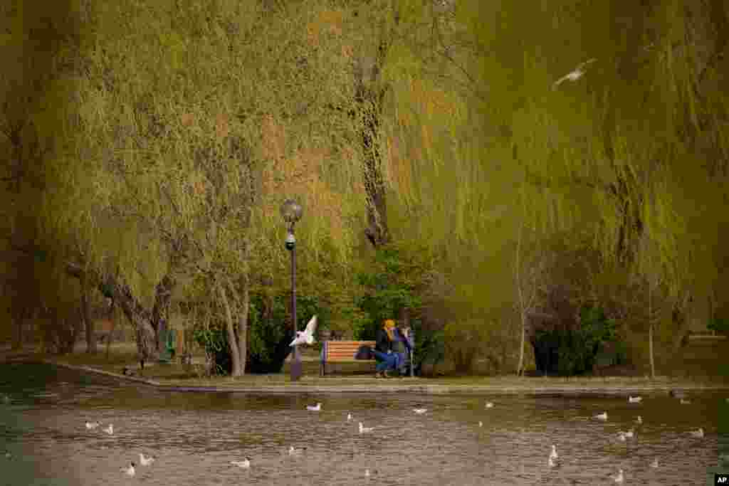 People sit on a bench in a park in Bucharest, Romania, March 18, 2023.