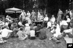 File - President Franklin Roosevelt reads to his guests as he and first lady Eleanor Roosevelt, at table, host a Labor Day picnic at their residence in Hyde Park, N.Y., Sept. 3, 1934.