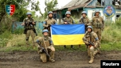 Ukrainian servicemen of the 35th Separate Brigade of Marines pose for a photograph with the Ukrainian flag in the liberated village of Storozheve, in Dontesk region, Ukraine, in the still image taken from a social media video released on June 12, 2023. 