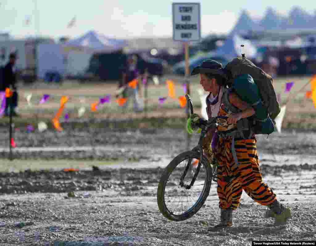A Burning Man participant walks her bike through the mud near the exit, after a severe rainstorm left tens of thousands of revelers attending the annual festival stranded in mud in Black Rock City, in the Nevada desert, Sept. 3, 2023.