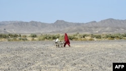 A woman carries water cans in a wheelbarrow at the Koh-e-Sabz area of Pakistan's southwest Baluchistan province, on Jan. 18, 2024.