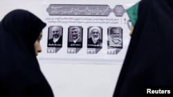 Iranian women stand near a paper showing the presidential candidates during the election to choose a successor to Ebrahim Raisi following his death in a helicopter crash, at the Iranian consulate in Najaf, Iraq, June 28, 2024. 
