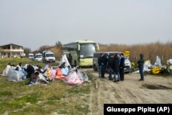 Recouverts de couvertures, les survivants d'un accident de bateau sont assis sur une plage près de Cutro, dans le sud de l'Italie, dimanche 26 février 2023.