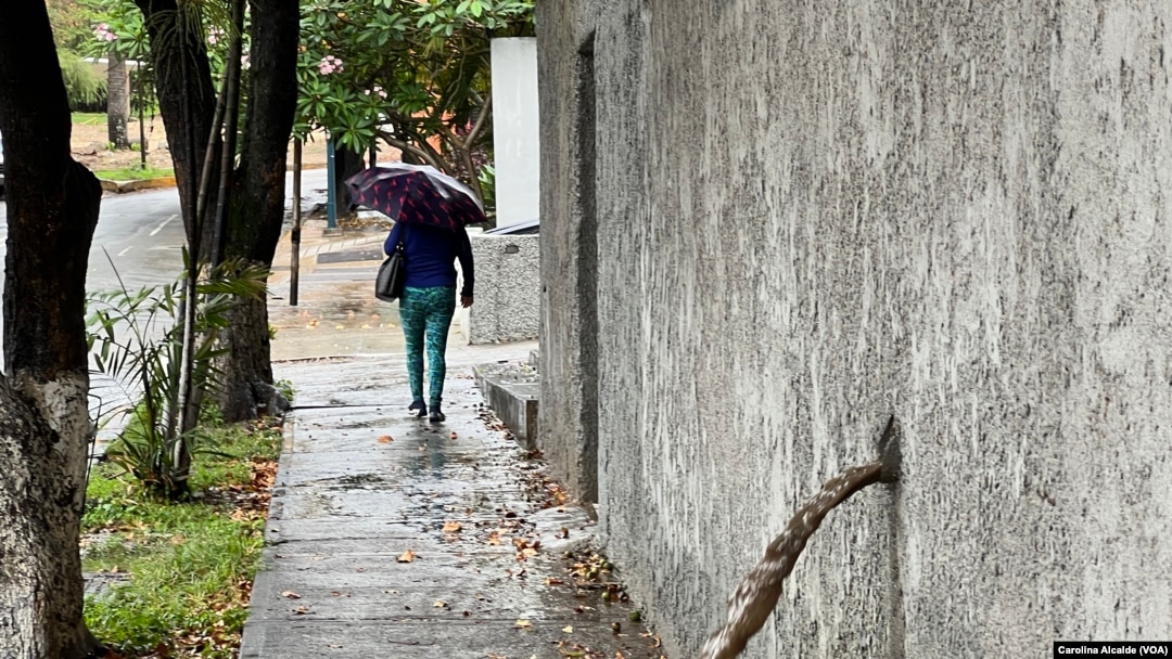 Una mujer se resguarda de la lluvia con un paraguas mientras camina por una calle del este de Caracas el 30 de mayo de 2023. 