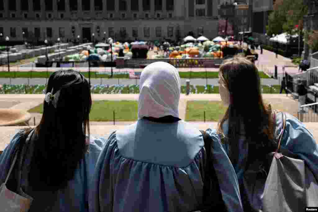 En la universidad de Columbia, estudiantes próximos a graduarse y en togas observan uno de los campamentos levantados en el campus para pedir el fin de la guerra.