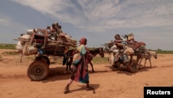 A Sudanese woman, who fled the conflict in Murnei in Sudan's Darfur region, walks beside carts carrying her family belongings upon crossing the border between Sudan and Chad in Adre, Chad, Aug. 2, 2023. 