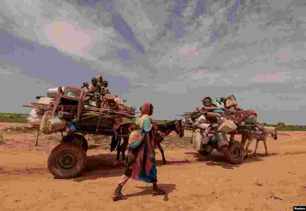 A Sudanese woman, who fled the conflict in Murnei in Sudan&#39;s Darfur region, walks beside carts carrying her family belongings upon crossing the border between Sudan and Chad, in Adre, Chad.