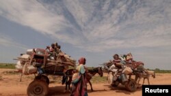 A Sudanese woman who fled the conflict in Murnei in Sudan&#39;s Darfur region walks beside carts carrying her family belongings upon crossing the border between Sudan and Chad, in Adre, Chad.