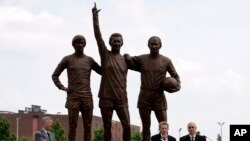 FILE - Ex-Manchester United players Bobby Charlton and Denis Law, bottom right, with Manchester manager Alex Ferguson, bottom left, speak in front of the statues of left to right, George Best, Law and Charlton, at Manchester, England, May 29, 2008.
