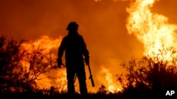 A firefighter is silhouetted by the flames of a fire on the outskirts of Villa Carlos Paz, Argentina, Oct. 10, 2023.