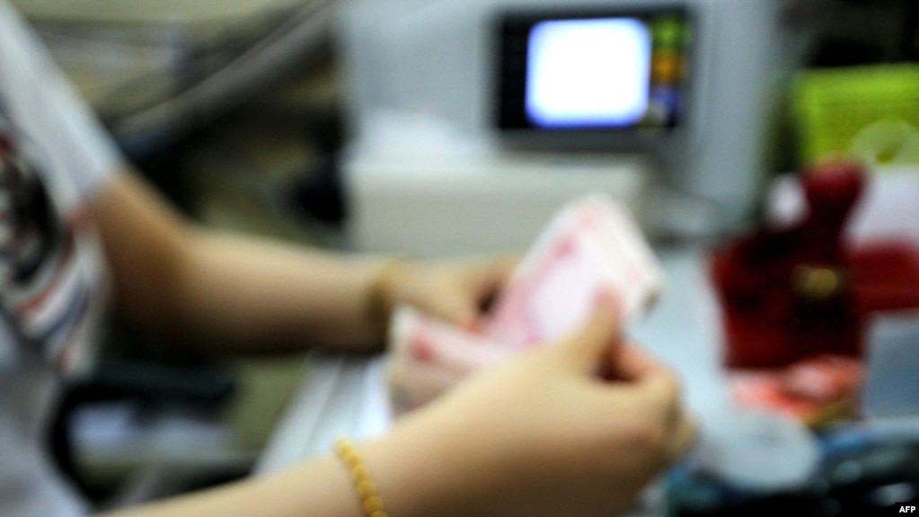 资料图片：这张摄于2015年8月11日的照片显示，在中国东部江苏省连云港的一家银行，一名出纳员正在清点人民币钞票。（法新社）(photo:VOA)