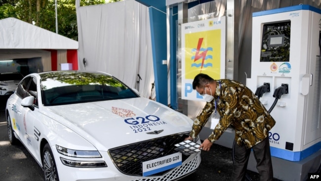 Seorang petugas sedang mengisi daya mobil listrik dalam perhelatan G20 di Nusa Dua, Bali, 25 Maret 2022. (Foto: Sonny Tumbelaka/AFP)