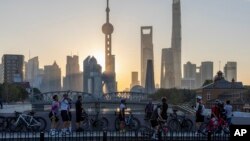 FILE - In this photo released by Xinhua News Agency, cyclists, some take selfie as they take rest against the sunrise skylines in Pudong, China's financial and commercial hub, in Shanghai, China, Nov. 3, 2023. (Wang Xiang/Xinhua via AP)