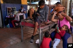 Carla Machado, right, waits with her children for her husband who cuts hair at a flea market in Maracaibo, Venezuela, July 22, 2024.