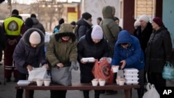 Elderly people wait to receive bread and hot food products from a humanitarian organization in the Saltivka neighborhood of Kharkiv, Ukraine, an area badly damaged by Russian shelling where most buildings are without electricity or water, Feb. 17, 2023.