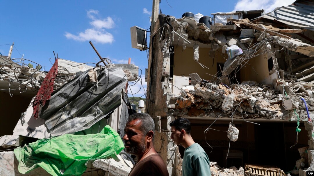 Palestinians walk past a damaged house after a raid by Israeli forces in the Nur Shams camp for Palestinian refugees in the occupied West Bank on April 21, 2024.