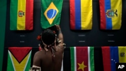 An indigenous man passes his hand over the Brazilian flag in a flag pavilion of the States parties to the Amazon Cooperation Treaty, during the Amazon Dialogue meetings at the Hangar convention center in Belem, Brazil, Aug. 6, 2023. 