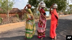 Tiga orang perempuan berjalan sambil membawa kendi berisi air minum pada suatu sore musim panas yang terik di Lalitpur, negara bagian Uttar Pradesh, India, Sabtu, 17 Juni 2023. (AP/Rajesh Kumar Singh)