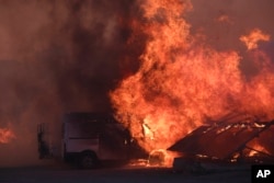 Flames burn a vehicle at a business during a fire in northern Athens, Aug. 12, 2024, as hundreds of firefighters tackle a major wildfire raging out of control on fringes of Greek capital.